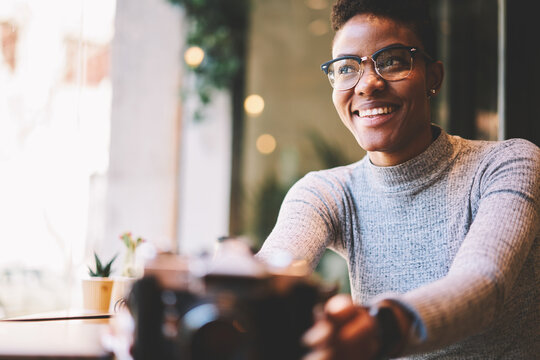 Cheerful attractive female photographer feeling happy getting new equipment for making pictures and earning money on photography, smiling hipster girl taking vintage camera spending time in cafe
