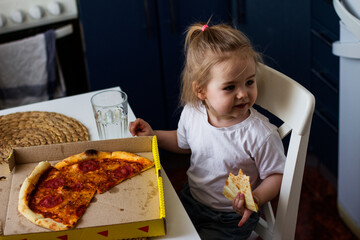 Little girl eating pizza in the kitchen at home.