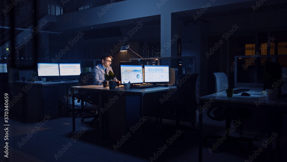 Poster working late at night in the office: businessman uses desktop computer, analyzing, using documents, 