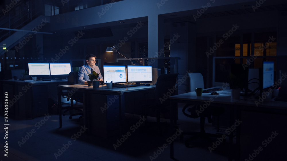 Poster working late at night in the office: businessman uses desktop computer, analyzing, using documents, 