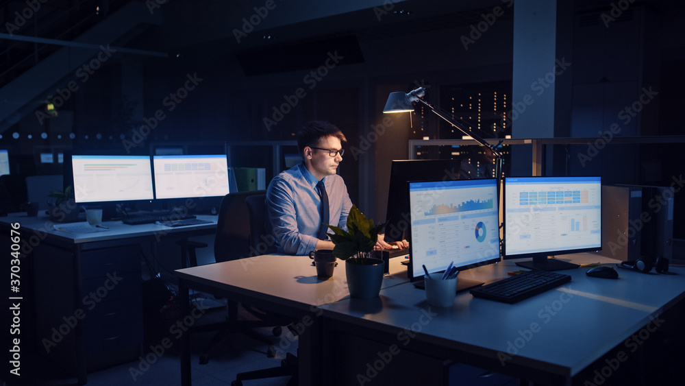 Poster working late at night in the office: businessman uses desktop computer, analyzing, using documents, 