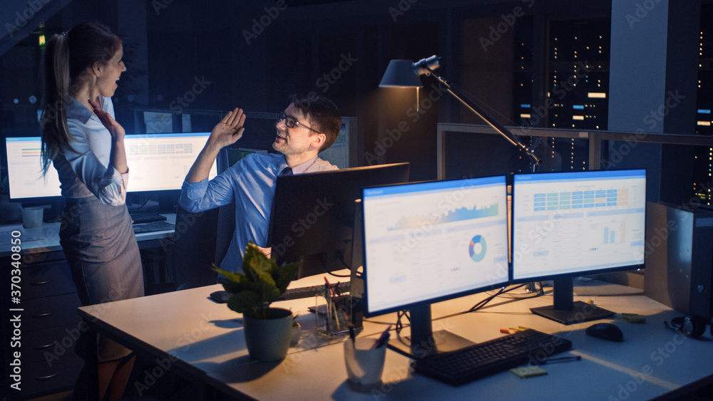 Poster late at night in modern office: office worker sitting and working at his desktop computer, discusses