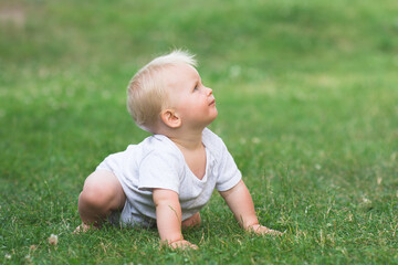 Little baby is crawling on all fours in the garden,  baby crawling on green grass and looking up, banner copy space