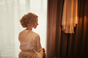 Beautiful bride standing near the window and smiling. Wedding Day