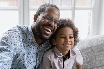 Overjoyed young african American dad and small boy child hug show love and affection in relationship, smiling biracial father and little son laugh joke, enjoy happy family weekend at home together