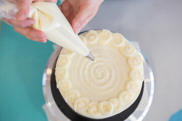 Woman pastry chef decorating cream and cheese cake in bakery shop.Decorating cake with a pastry bag with cream.Top view.Celebrations food concept