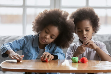 Little african american girl and boy kids have fun play with plasticine or modeling clay at home...