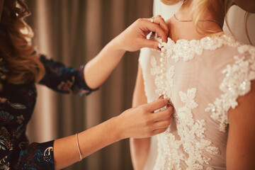 Wedding. Bridesmaid preparing bride for the wedding day. Bridesmaid helps fasten a dress before the...