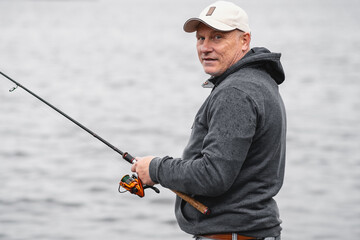 A fisherman in a baseball cap with a fishing rod in his hands smiles. Concept of healthy outdoor recreation.