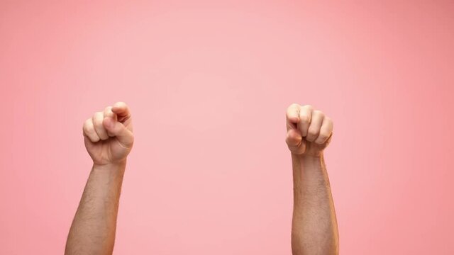 young man holding hands up pointing fingers and making thumbs up sign on pink background