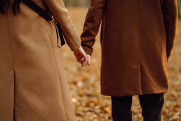 Young couple in love walking in the park on a autumn day. Enjoying time together. Stylish and loving couple enjoying each other in the autumn forest. 