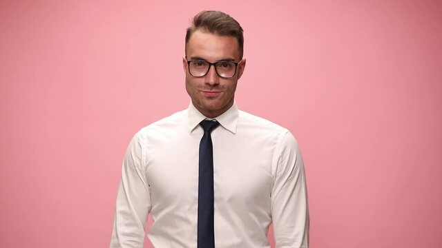 sexy elegant man in white shirt wearing glasses tilting head in both sides and smiling on pink background