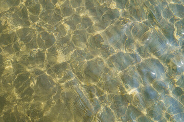 Fototapeta na wymiar Close view onto bottom of sea near coastline, that colored by sun in gold tones. There are shallow water, small playing waves & underwater sand