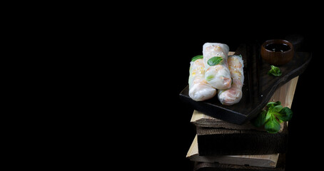 Spring rolls with roasted shrimps, vegetables and noodles wrapped in rice paper against the black background