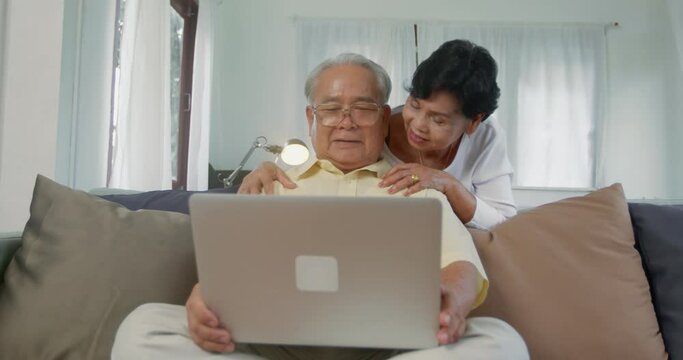 Slow motion of old couple talking during looking on laptop on sofa, happy family senior use free time to surf internet and play computer at home, high technology and global network with old people