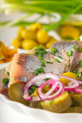 Slices of pickled herring with red onion, fermented cucumber, fried potatoes, olives. Close-up