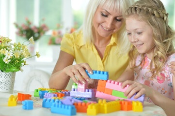 Obraz na płótnie Canvas Little daughter and mother playing with colorful plastic blocks at home