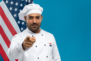 Young male chef of restaurant in white uniform with vote insignia on chest