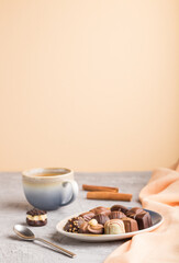 Different chocolate candies and a cup of coffee on a gray and orange background. side view, selective focus, copy space.
