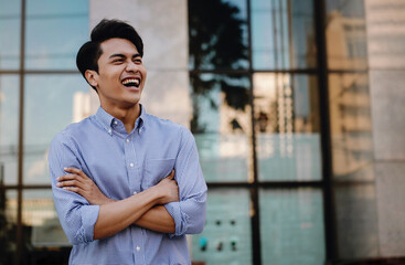 Portrait of Laughing Young Asian Businessman in the City. Crossed Arms and looking away. a Happy Friendly Man