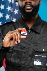 Hand of bearded African male security in black uniform showing you vote insignia