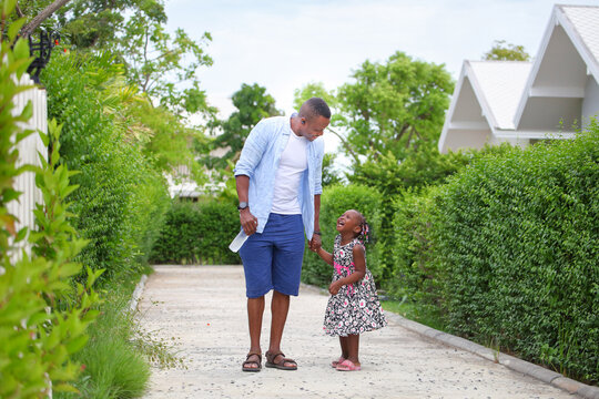 African American Father Is Holding His Little Daughter Hand And Having A Good Time Together While Walking Outside The House Around The Neighborhood During Summer Time