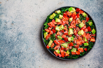 Kale salad with tomatoes and avocado in black plate, top view, copy space.