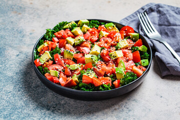 Kale salad with tomatoes and avocado in black plate. Healthy raw vegan lunch concept.