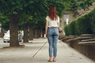 Blind woman is walking on the sidewalk in city. Woman using a white cane.