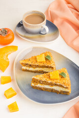 Homemade cake with persimmon and pumpkin and a cup of coffee on a white wooden background with orange textile. side view, close up.