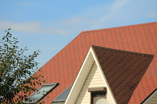 icon roof with new brown roofing tiles on residential property. banner on  roof for roofers. concept for roof housetop. roof structure with attic skylights, gutter system, windows protection and fence