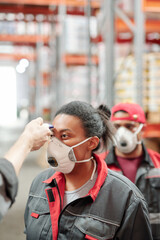 Worker of warehouse in respirator and workwear having her temperature measured