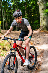 Young man biking in forest on red bike
