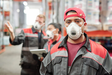 Middle aged Latino man in workwear and protective respirator looking at you