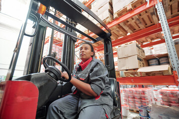 Young mixed-race woman in workwear sitting by steer inside industrial machine