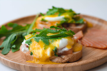 Poached eggs Benedict with Hollandaise sauce, smoked salmon, arugula on toasted bread. Wooden plate, white background.