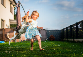 Baby girl running with beagle dog in garden on summer day. Domestic animal with children concept.