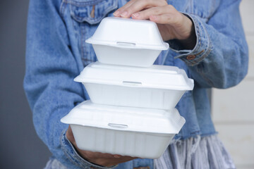 Woman's hands holding takeaway foam lunch boxes. Single use food containers, close up.
