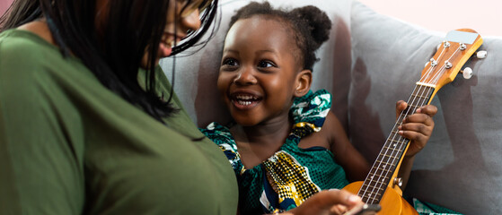 Happy Mom with her daughter playing guitar and singing together at home, happy family