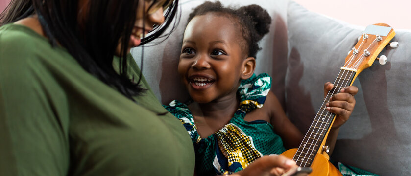 Happy Mom with her daughter playing guitar and singing together at home, happy family
