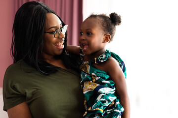 Happy young African American mother having fun with daughter child girl playing and hugging in...
