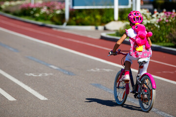 Fototapeta na wymiar Little girl in pink suit rides a bicycle
