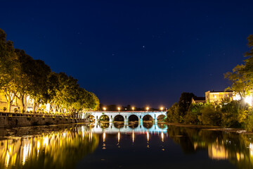 Fototapeta premium Vue nocturne sur le Pont Tibère et sa réflexion sur les eaux du fleuve Vidourle à Sommières (Occitanie, France)