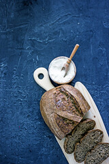 Loaf of homemade sourdough bread cut into slices on a wooden board on a dark stone table, top view, flat lay, vertical background, top-down food