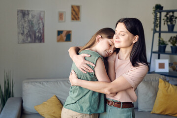 Young loving mother embracing her cute affectionate daughter in home environment