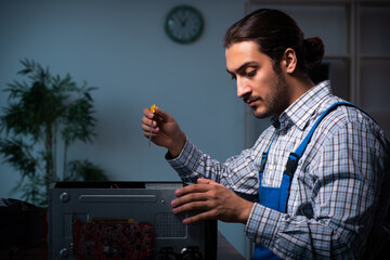 Young male technician repairing computer in workshop at night