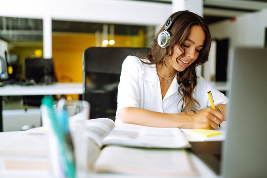 Young woman student wear wireless headphone study online. She learn language listen lecture watch webinar write notes look at laptop, distant education. Video call self-isolation during ncov situation