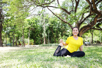 Smiling Asian young woman in yellow sportwear sitting and doing yoga for meditation for create concentration and calm the mind on grass field after exercise in the natural light garden.