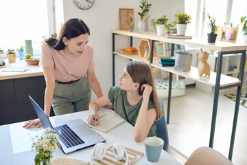 Young mother bending over desk where her teenage daughter studying