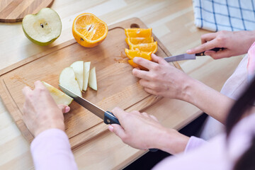 Hands of two young contemporary females with knives slicing fresh fruits